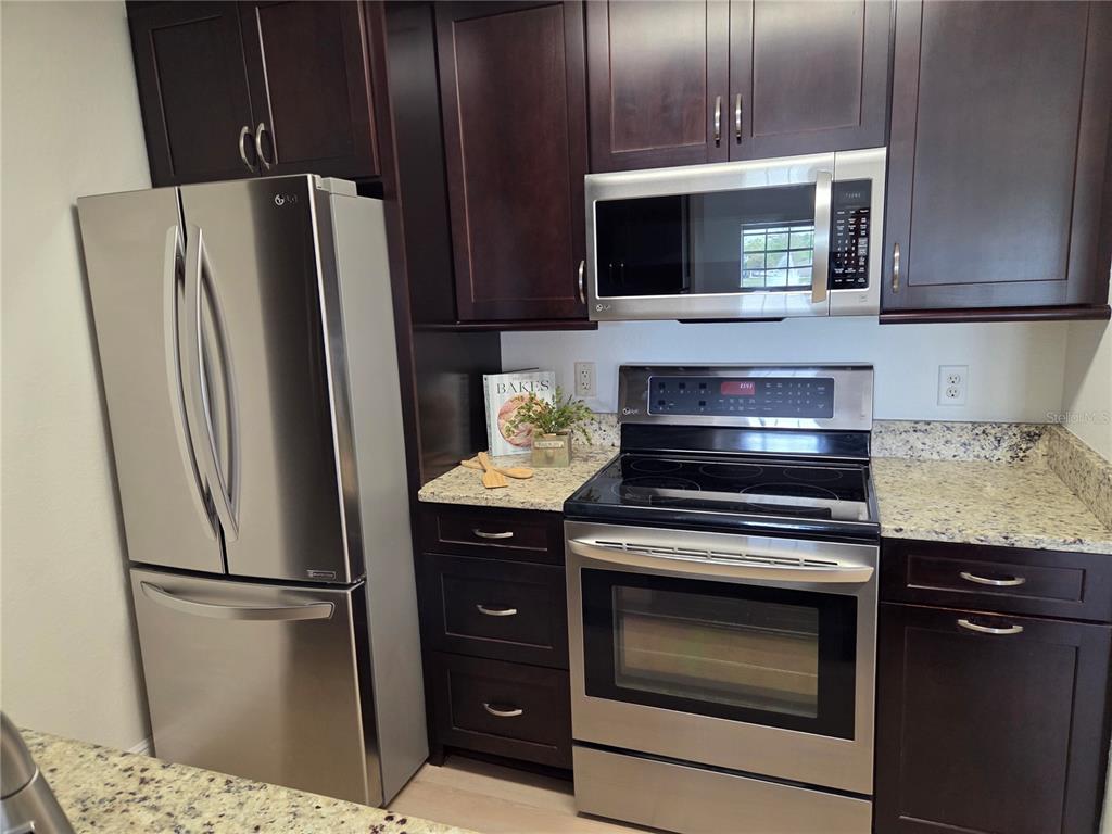 8905 Manor Loop, Unit 205 Lakewood Ranch, FL 34202 - Photo 13 of 30 a kitchen with granite countertop a refrigerator stove and microwave