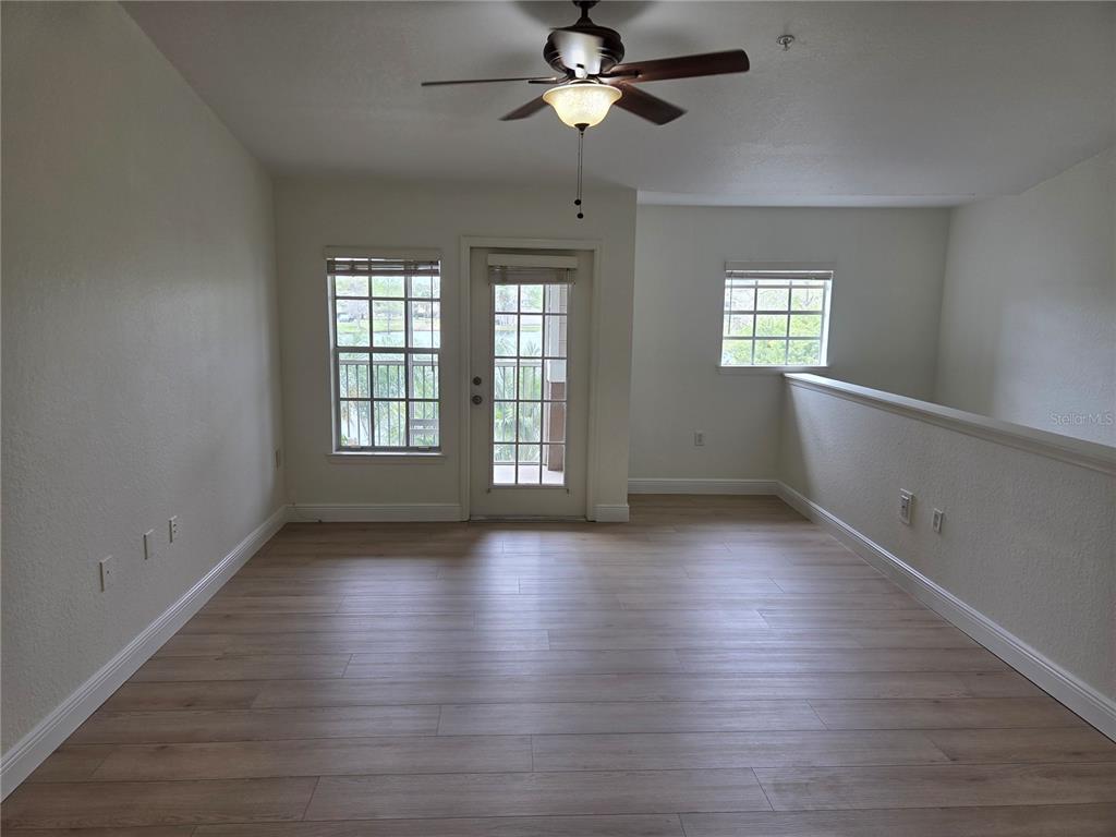 8905 Manor Loop, Unit 205 Lakewood Ranch, FL 34202 - Photo 7 of 30 an empty room with wooden floor chandelier fan and windows