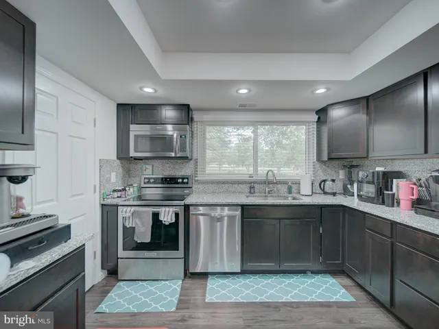 a kitchen with stainless steel appliances granite countertop wooden cabinets a sink dishwasher a stove and a refrigerator with wooden floor