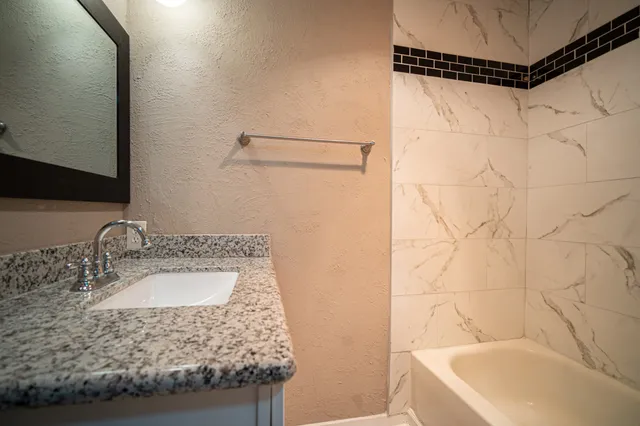 a bathroom with a granite countertop sink a mirror and shower