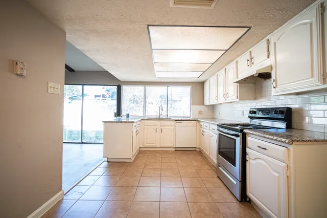 a large kitchen with stainless steel appliances granite countertop a stove a sink and white cabinets
