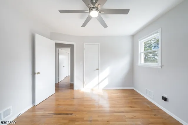 an empty room with wooden floor chandelier fan and windows