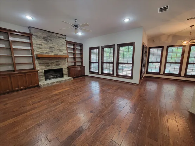 a view of an empty room with wooden floor fireplace and a window