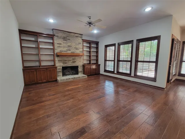 an empty room with wooden floor fireplace and windows