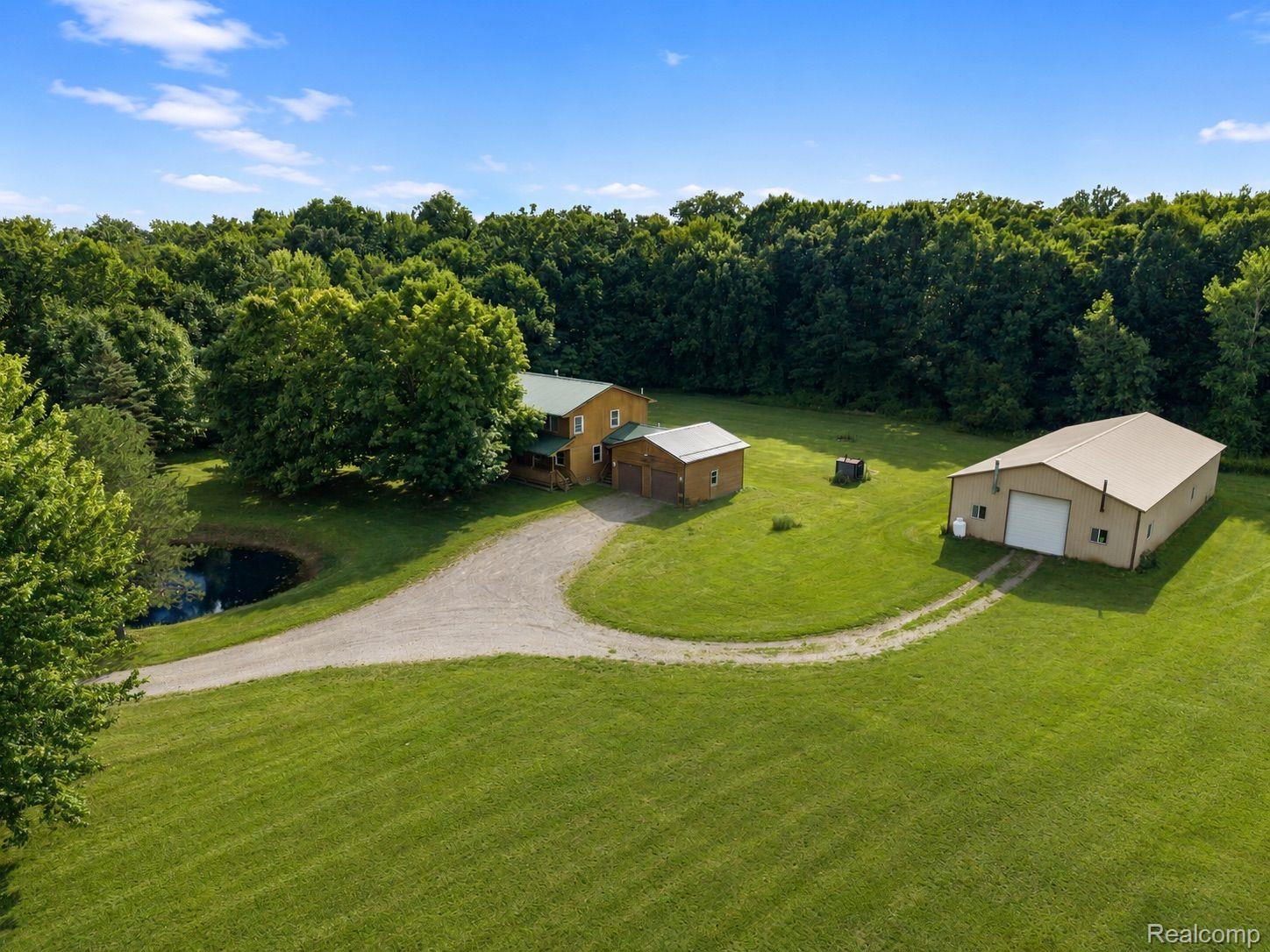 76565 McFadden Road Armada, MI 48005 - Photo 75 of 95 Expansive property featuring a gravel driveway, a large detached outbuilding, a smaller detached shed, a pond, and mature trees