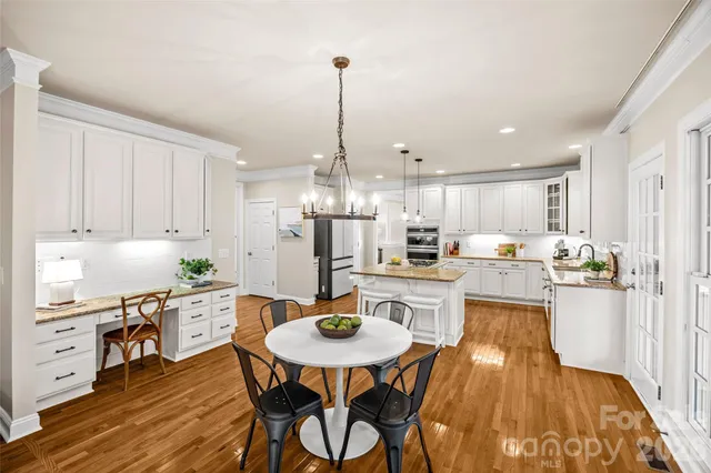 a kitchen with stainless steel appliances kitchen island granite countertop a dining table chairs and white cabinets