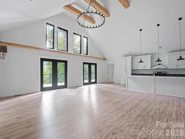 a view of an empty room with wooden floor and a kitchen