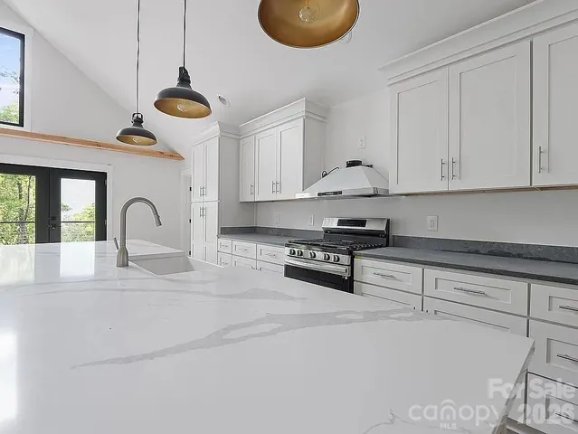 a kitchen with stainless steel appliances granite countertop a stove a sink a kitchen island with a stove and white cabinets