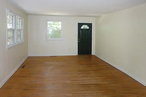 a view of an empty room with wooden floor and a window