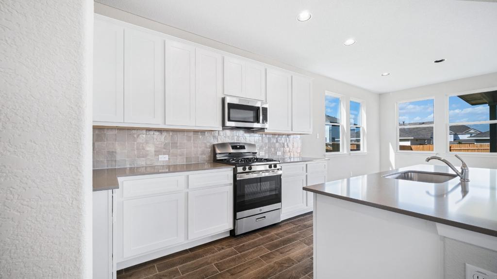 208 Stein Road Georgetown, TX 78626 - Photo 13 of 30 Kitchen with appliances with stainless steel finishes, recessed lighting, decorative backsplash, dark wood finished floors, and white cabinets