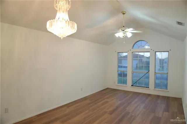 an empty room with wooden floor chandelier fan and windows