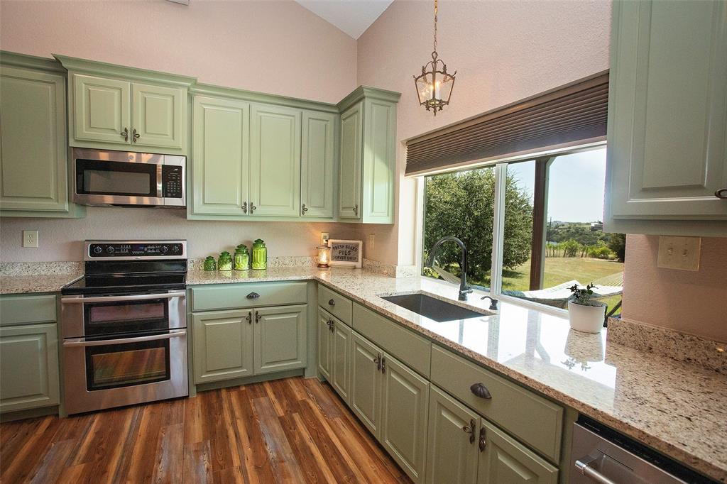 7060 Hells Gate Loop Strawn, TX 76475 - Photo 33 of 40 Kitchen featuring stainless steel appliances, green cabinets, vaulted ceiling, and dark wood-style flooring