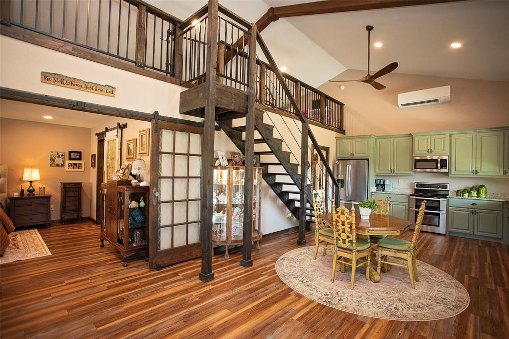 7060 Hells Gate Loop Strawn, TX 76475 - Photo 35 of 40 Dining area featuring high vaulted ceiling, a wall mounted air conditioner, a barn door, stairway, and dark wood-style flooring