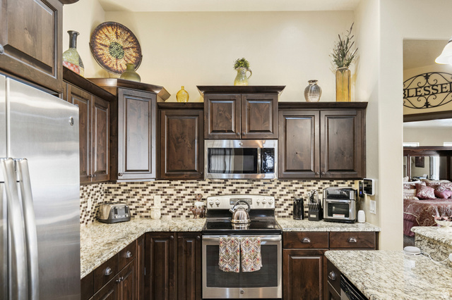 210 Talon Court Ivins, UT 84738 - Photo 21 of 60 Kitchen featuring dark wood finish cabinets, stainless steel appliances, light stone countertops, and backsplash