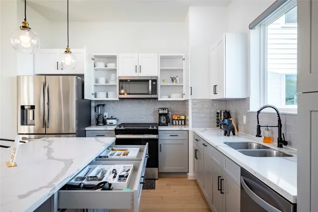 a kitchen with stainless steel appliances a sink a stove a refrigerator white cabinets a window and a kitchen island