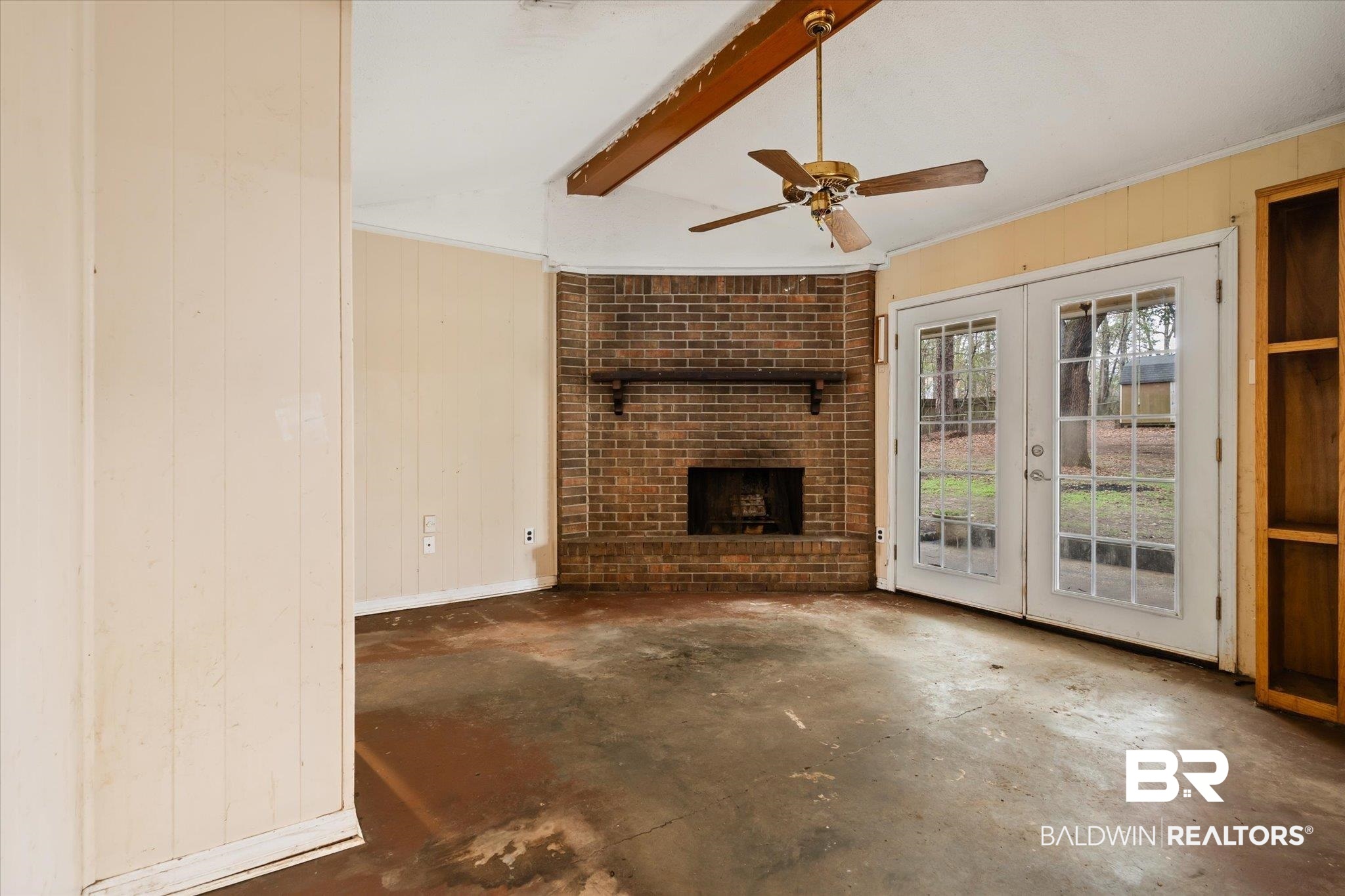 3541 Winston Drive Semmes, AL 36575 - Photo 8 of 20 Unfurnished living room with wooden walls, lofted ceiling with beams, unfinished concrete floors, french doors, and a brick fireplace