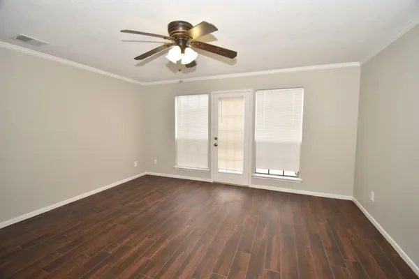 an empty room with wooden floor chandelier fan and windows