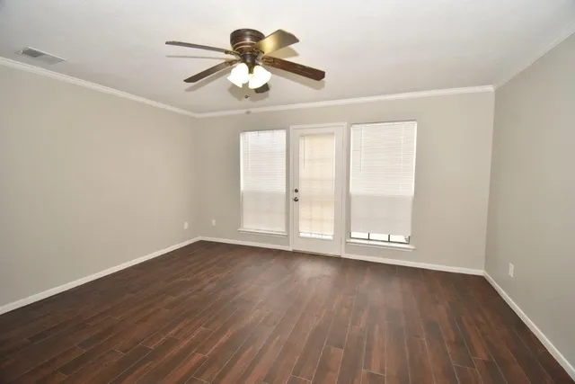 an empty room with wooden floor chandelier fan and windows