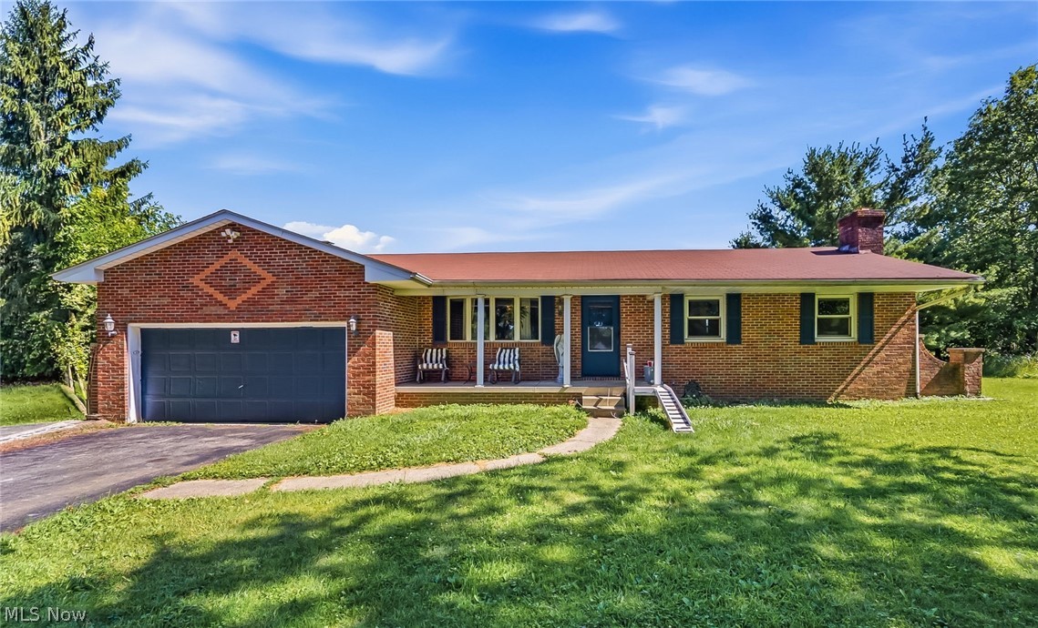 6890 Refugee Road Pickerington, OH 43147 - Photo 1 of 49 Brick ranch-style home featuring a two-car garage with a dark gray door, a covered front porch with white columns, and a reddish-brown roof