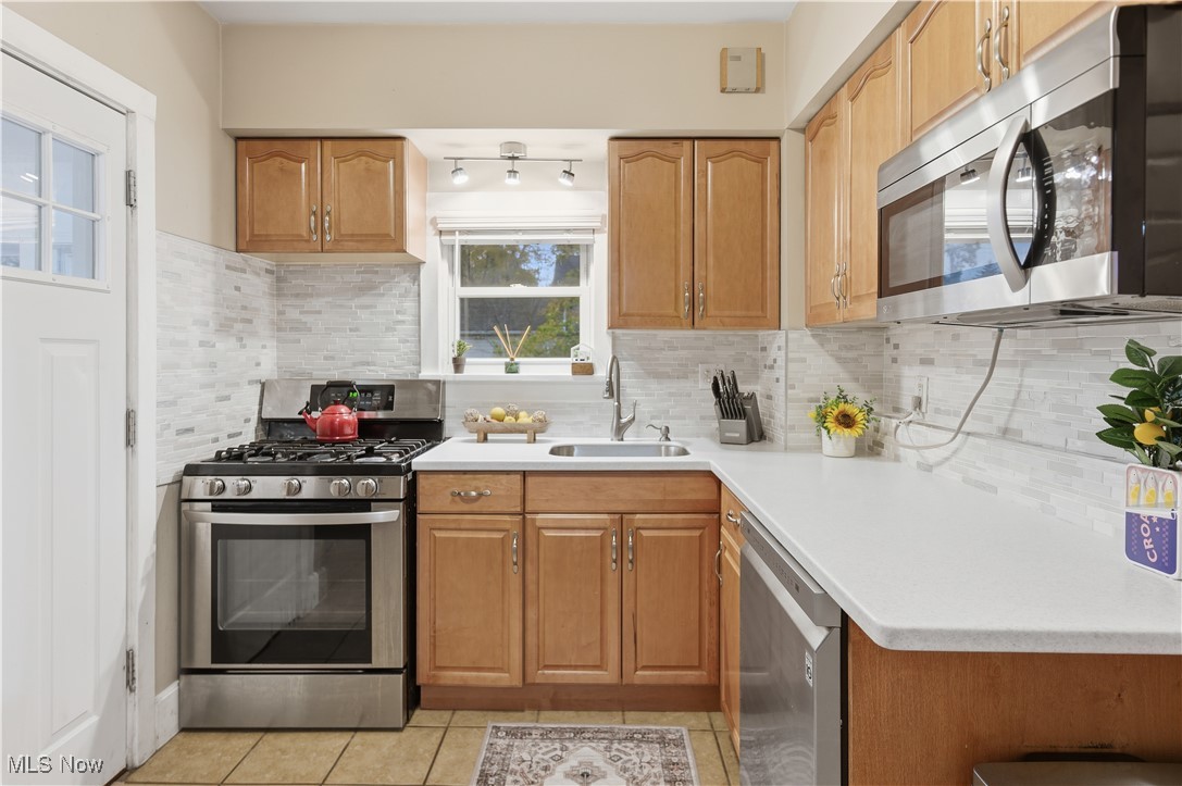 1017 Spring Road Cleveland, OH 44109 - Photo 15 of 47 Kitchen with stainless steel appliances, backsplash, light countertops, light tile patterned flooring, and brown cabinetry