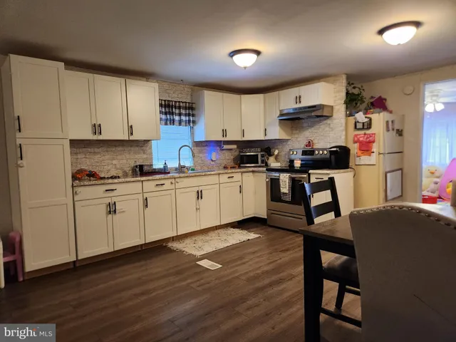 a kitchen with stainless steel appliances granite countertop a sink dishwasher a stove refrigerator and white cabinets with wooden floor