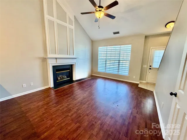 an empty room with wooden floor fan and windows