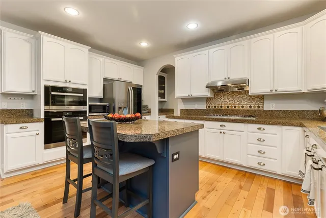 a kitchen with stainless steel appliances kitchen island granite countertop a table chairs sink refrigerator and cabinets