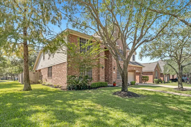 a brick house with a big yard plants and large trees