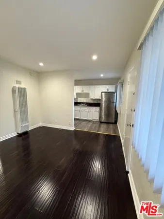 a view of an empty room with wooden floor and a kitchen