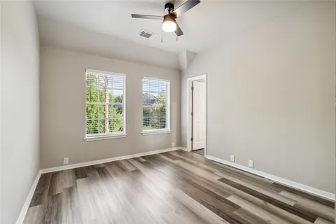 an empty room with wooden floor fan and windows