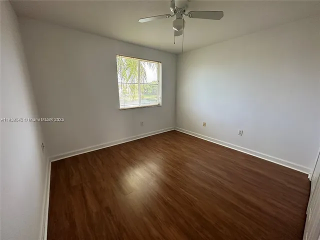 an empty room with wooden floor chandelier fan and windows