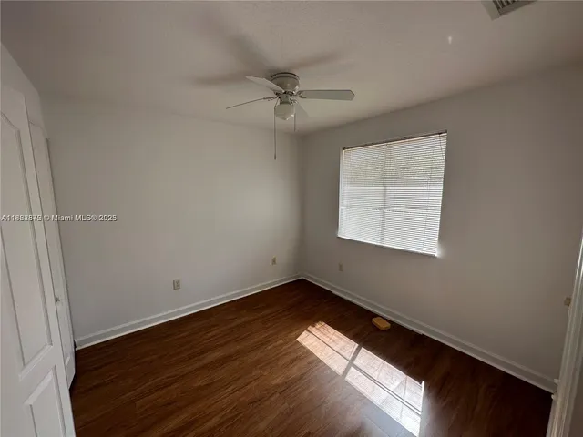 an empty room with wooden floor chandelier fan and windows