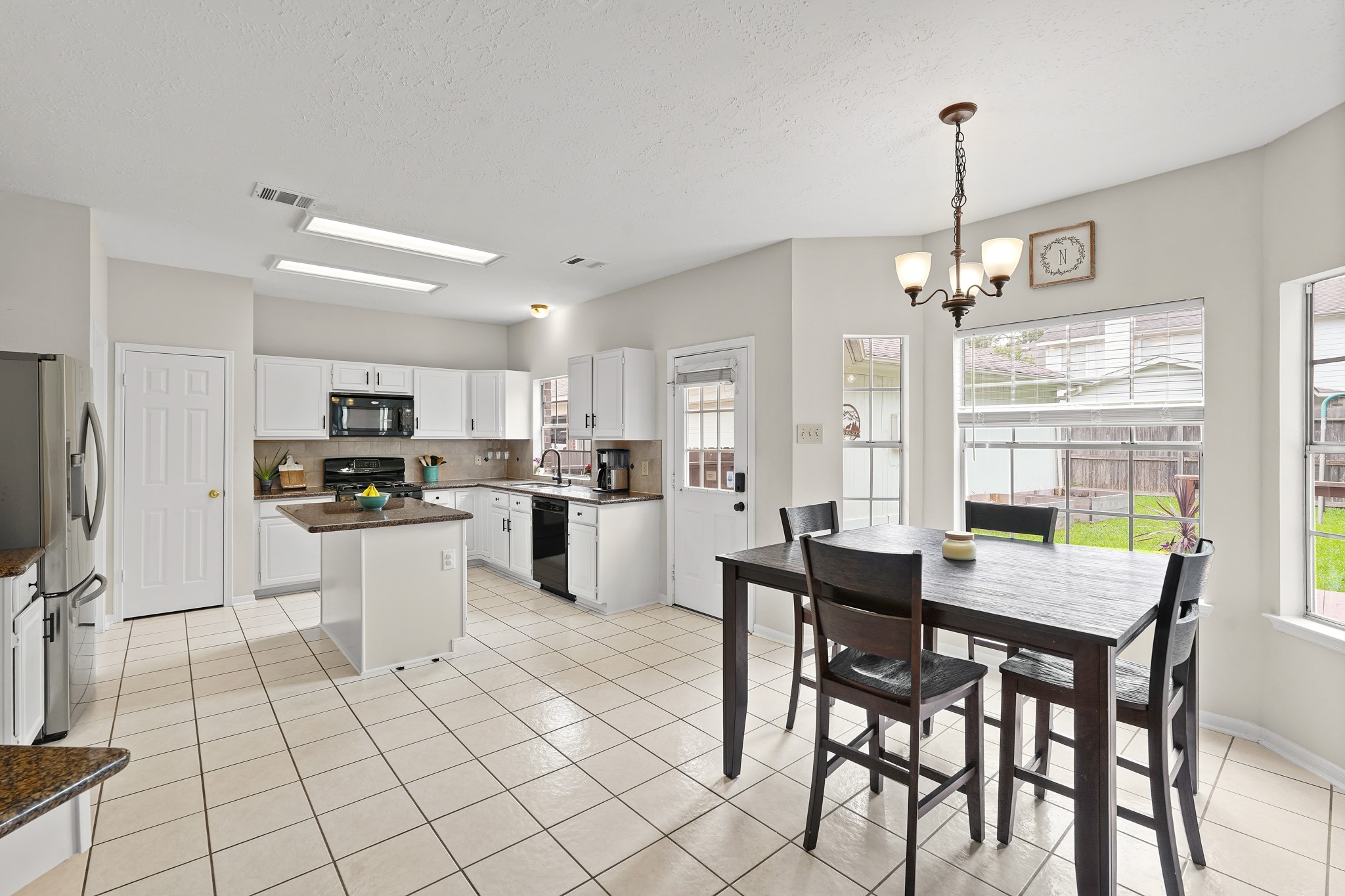16114 Kintyre Point Road Houston, TX 77095 - Photo 28 of 44 This bright kitchen features white cabinetry, modern appliances, and a central island. The adjacent dining area offers ample natural light from large windows, creating a welcoming space for meals.