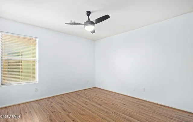 an empty room with wooden floor ceiling fan and windows