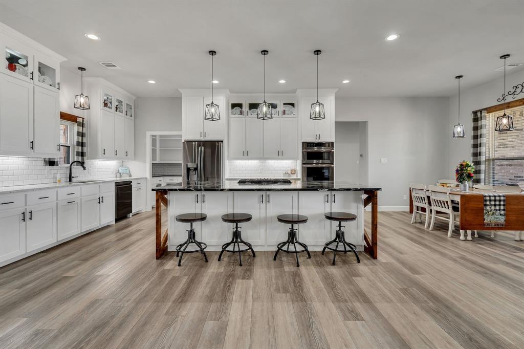 7739 Borth Road Sanger, TX 76266 - Photo 12 of 39 Dual tone kitchen with pendant lighting, glass fronted cabinets, a kitchen breakfast bar, decorative backsplash, and stainless steel appliances