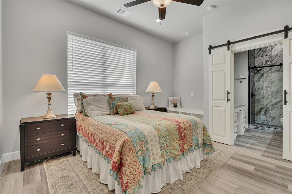 7739 Borth Road Sanger, TX 76266 - Photo 24 of 39 Guest bedroom featuring a barn door, connected bathroom, light wood-style flooring, and ceiling fan