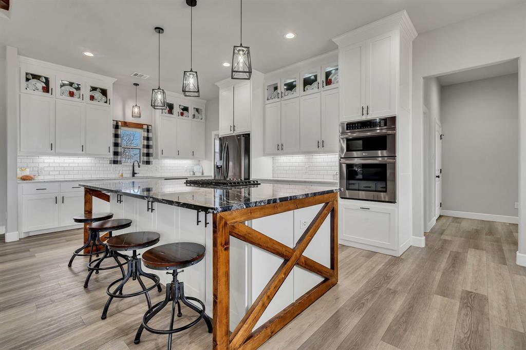 7739 Borth Road Sanger, TX 76266 - Photo 7 of 39 Kitchen with glass fronted cabinets, light wood finished floors, dark stone counters, a kitchen bar, and stainless steel appliances