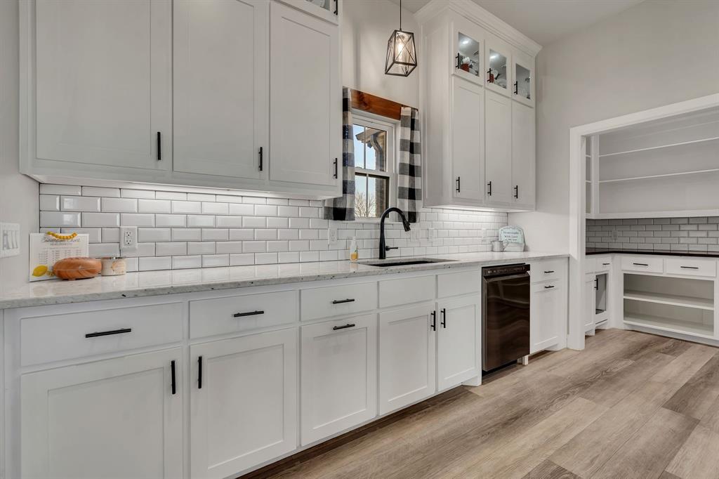 7739 Borth Road Sanger, TX 76266 - Photo 8 of 39 Kitchen with white cabinets, light stone counters, glass insert cabinets, and decorative light fixtures