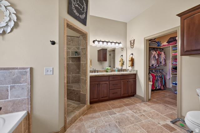 4635 East Sunny Acres Lane Moab, UT 84532 - Photo 51 of 56 Expansive bathroom featuring large-format tile flooring, a walk-in shower with tiled walls and a built-in bench, a double vanity with a stone countertop and wood-finish cabinetry, and a spacious walk-in closet with built-in shelving and hanging rods