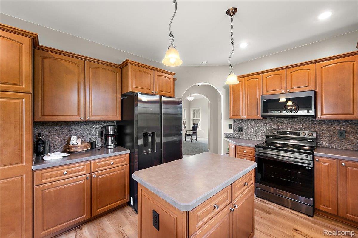 5035 Hidden Ridge Road Metamora, MI 48455 - Photo 11 of 62 Kitchen featuring wood-finish cabinetry, a central island, stainless steel appliances, a mosaic tile backsplash, and pendant lighting