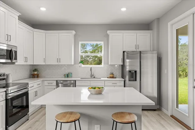 a kitchen with stainless steel appliances a stove a sink a refrigerator and white cabinets with wooden floor