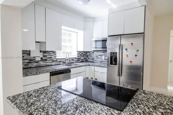 a kitchen with stainless steel appliances granite countertop a refrigerator a stove a sink and white cabinets