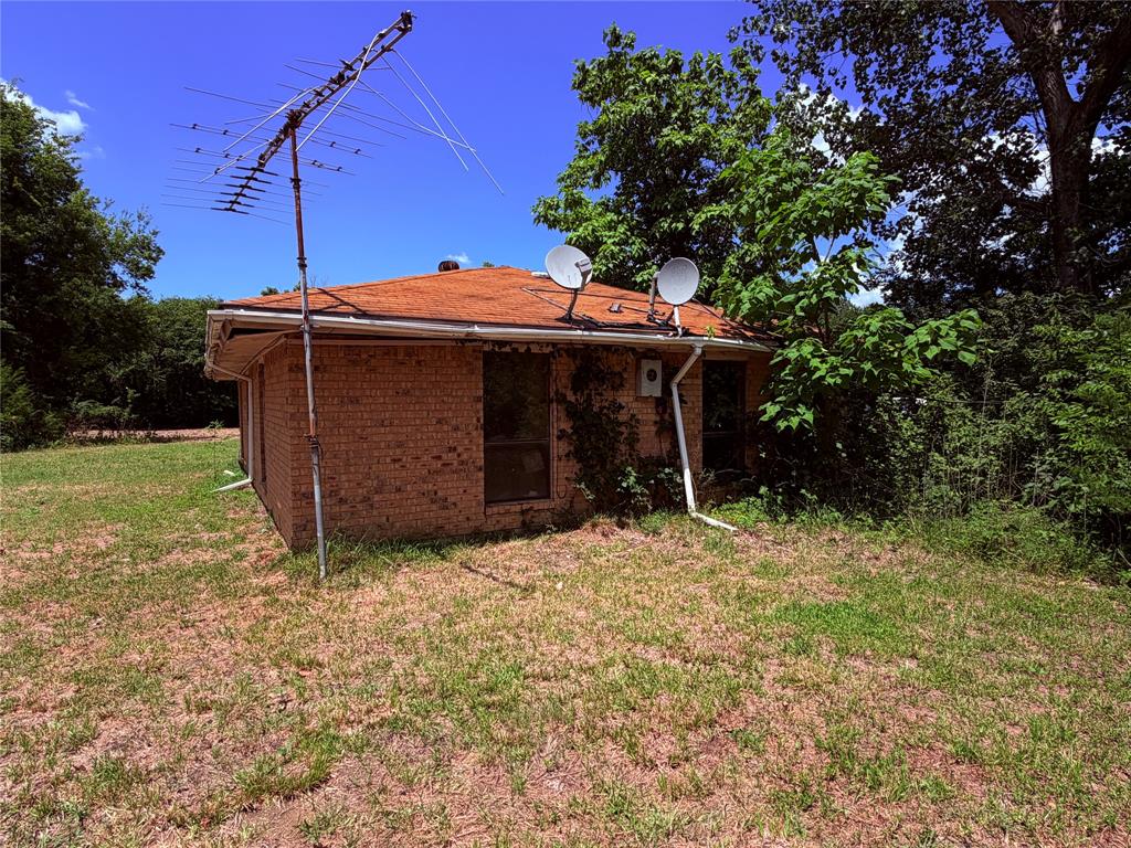 690 County Road Brookston, TX 75421 - Photo 3 of 10 Brick exterior with a brown shingled roof, white gutters, and mature trees surrounding the property