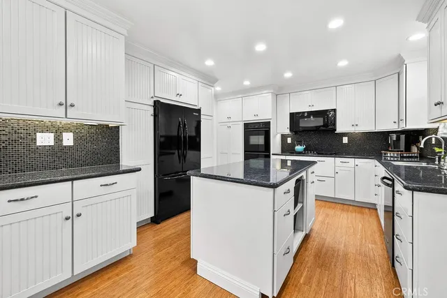 a kitchen with granite countertop a refrigerator a stove top oven a sink dishwasher and white cabinets with wooden floor