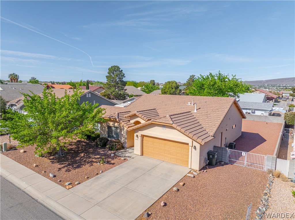 3973 Prairie View Drive Kingman, AZ 86409 - Photo 3 of 34 The property features a concrete driveway leading to an attached garage, a low-maintenance front yard with decorative rock landscaping and a mature tree, and a tiled roof