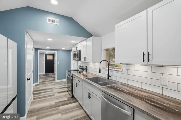 a large white kitchen with a sink and dishwasher a stove top oven with wooden floor