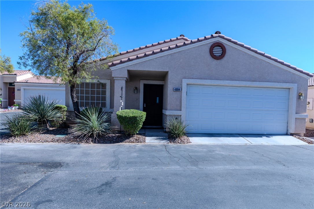A terracotta-tiled roof crowns this residence, featuring stucco walls and desert landscaping with an attached garage.