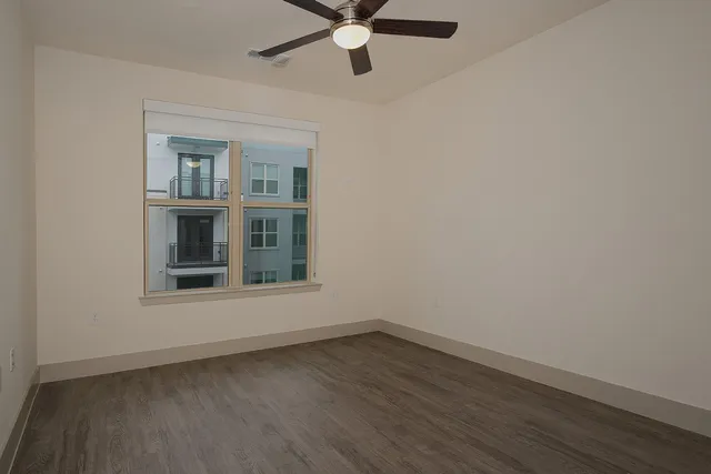 an empty room with wooden floor chandelier fan and windows