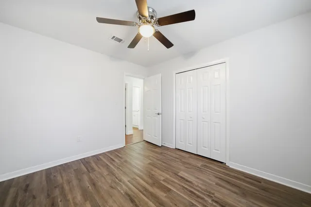 an empty room with wooden floor ceiling fan and windows