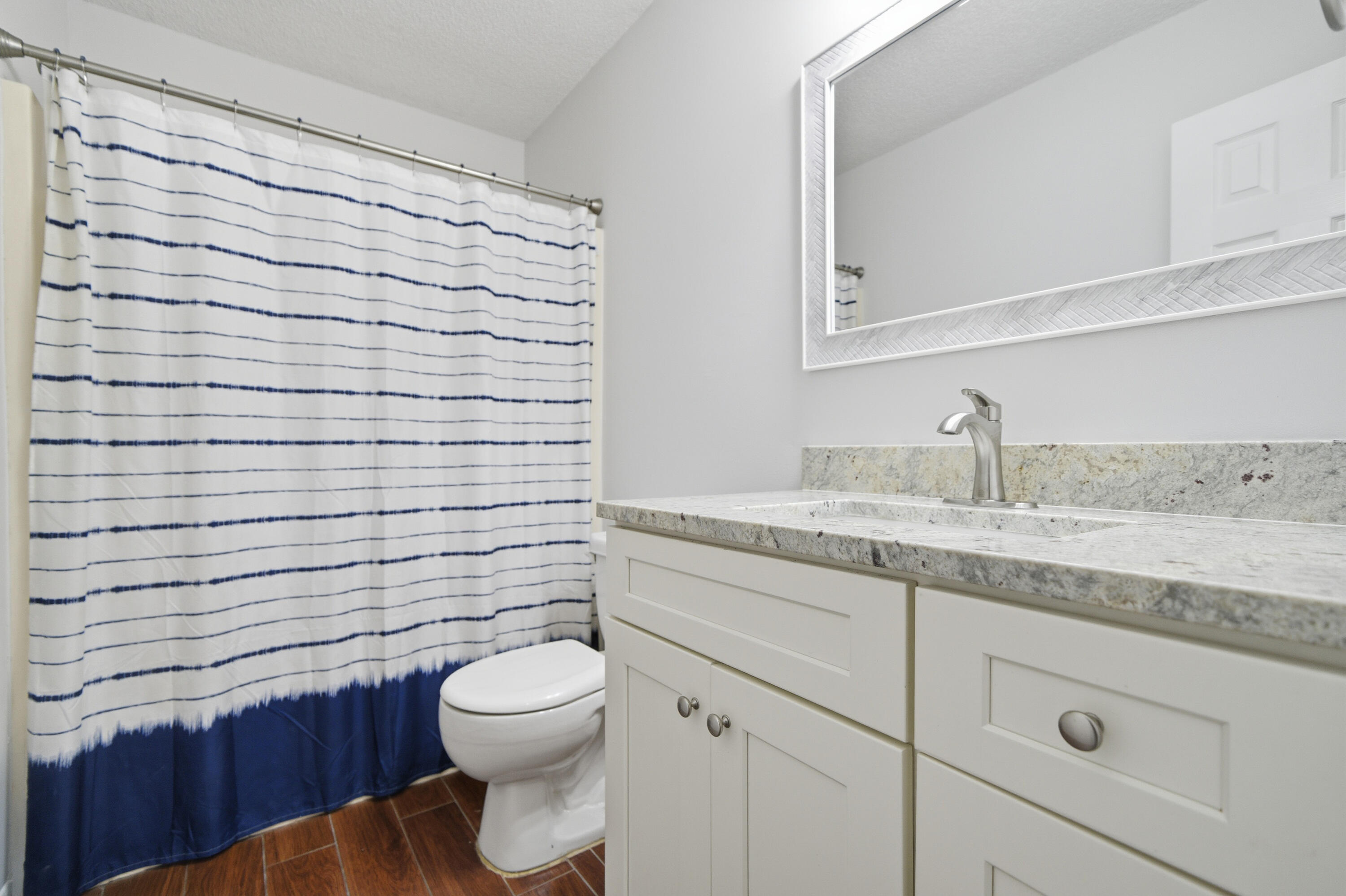 411 Ashley Drive Crestview, FL 32536 - Photo 35 of 44 a bathroom with a granite countertop toilet a sink a mirror and shower curtain
